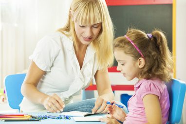 Cute little girl having speech therapy with young female speech/language therapist in a office. Therapist showing illustration to hear how she pronouncing some letters. Selective focus to young woman. They are drawing together also.